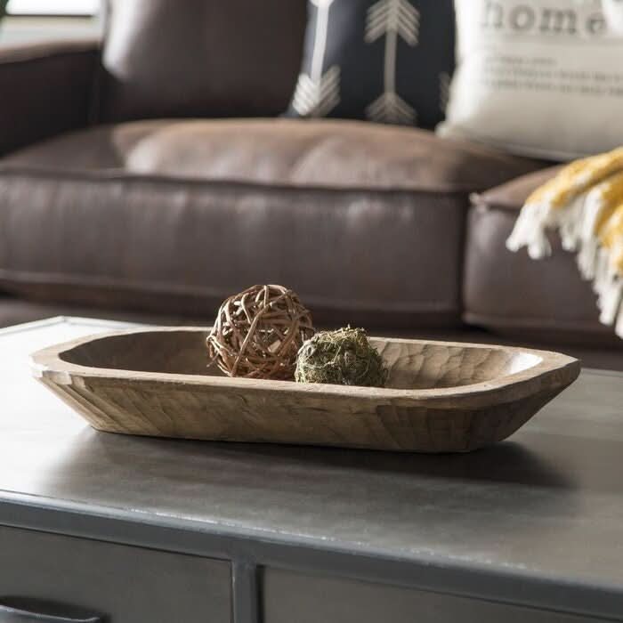 Wooden dough bowl with decorative spheres on a coffee table in a living room setting.